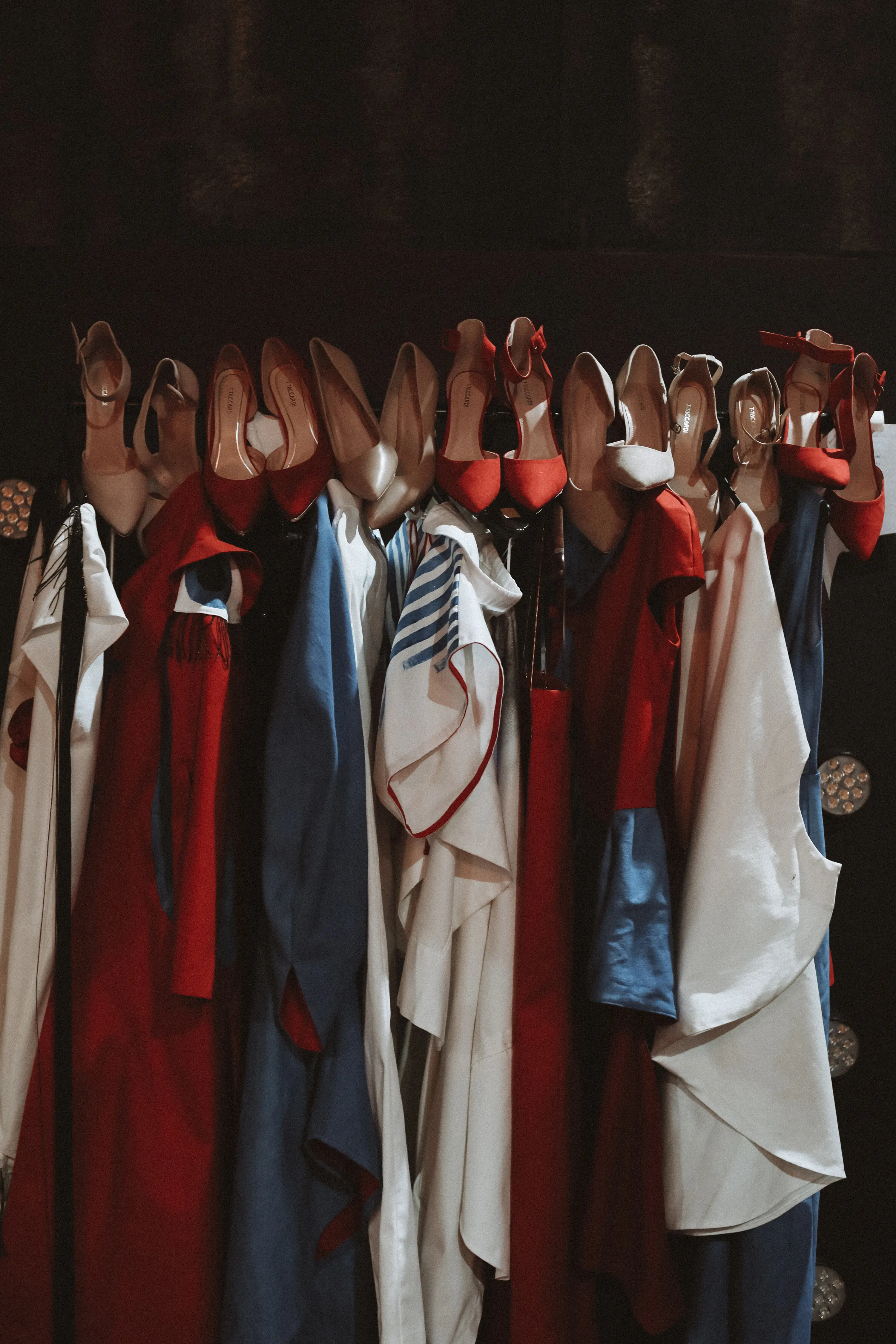 Im Backstage-Bereich hängen verschiedene Mode-Outfits und High Heels in einer Reihe.